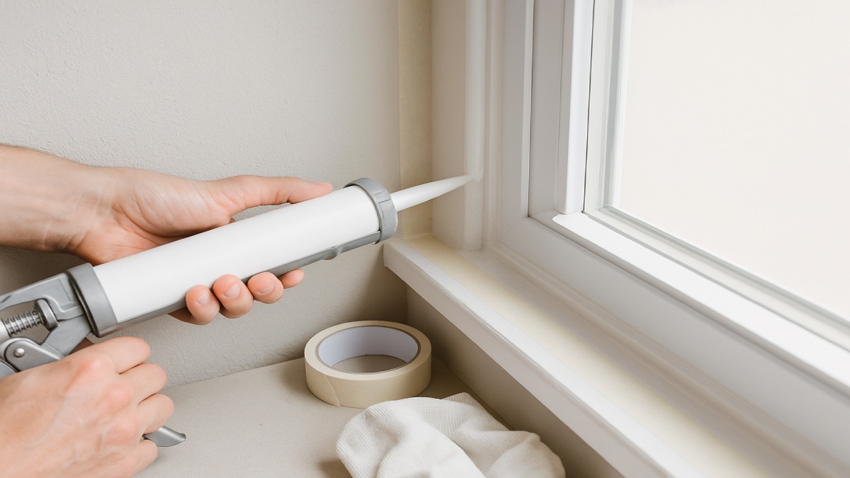 Applying a smooth bead of caulk along interior window trim to stop drafts
